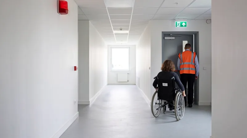 Een BHV'er begeleidt iemand in een rolstoel naar de nooduitgang